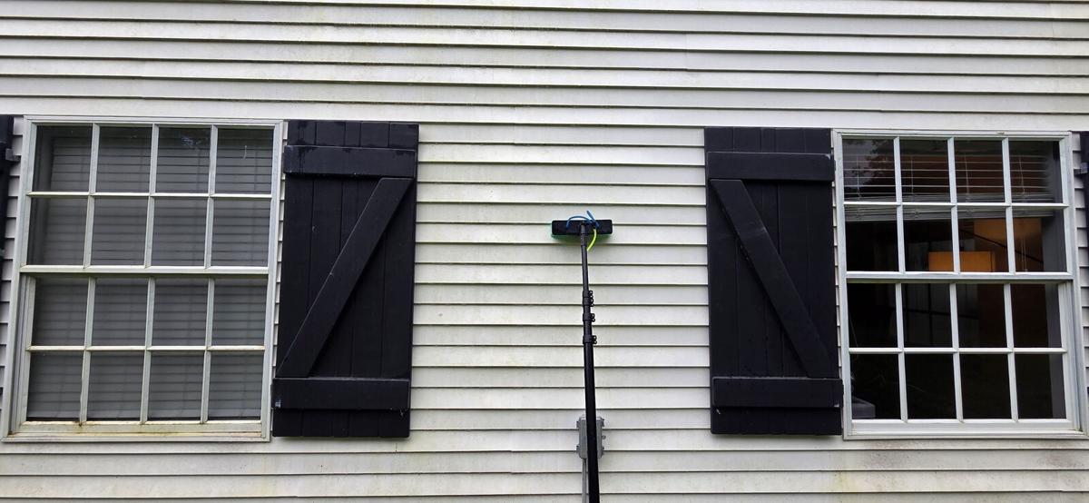 Squeegee pole against a gray-sided home with black shutters during a window clean