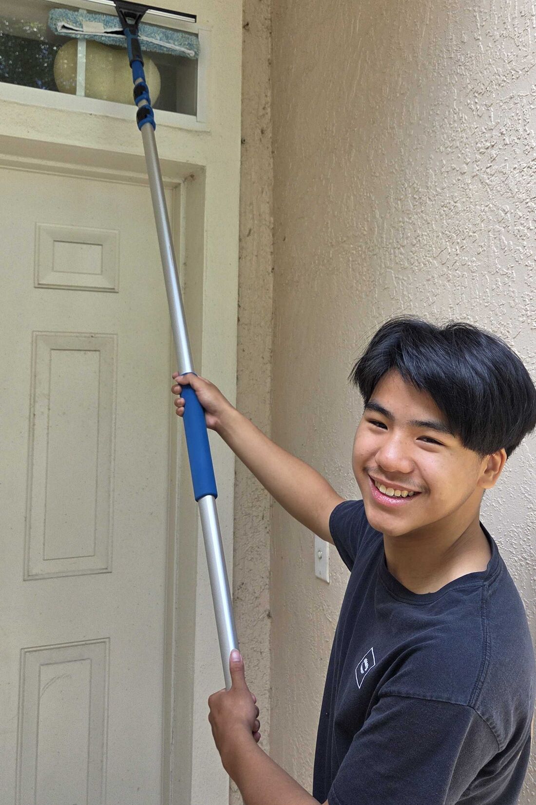 Seaton, owner of Seatown Window & Wash, smiling while cleaning a front-door window with a squeegee pole